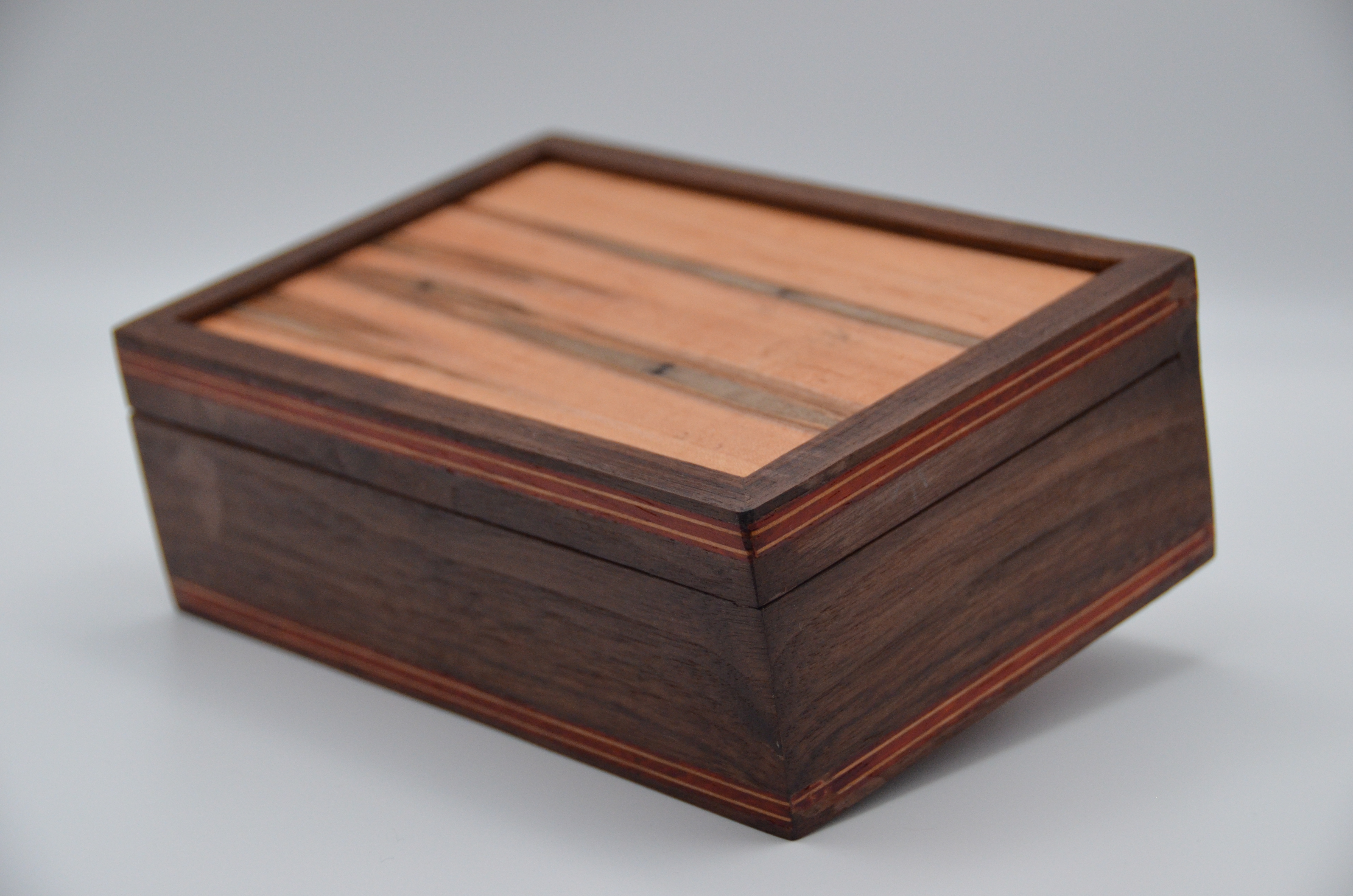 Front view of a small wooden box on a light surface, showing marquetry inlay on the lid.