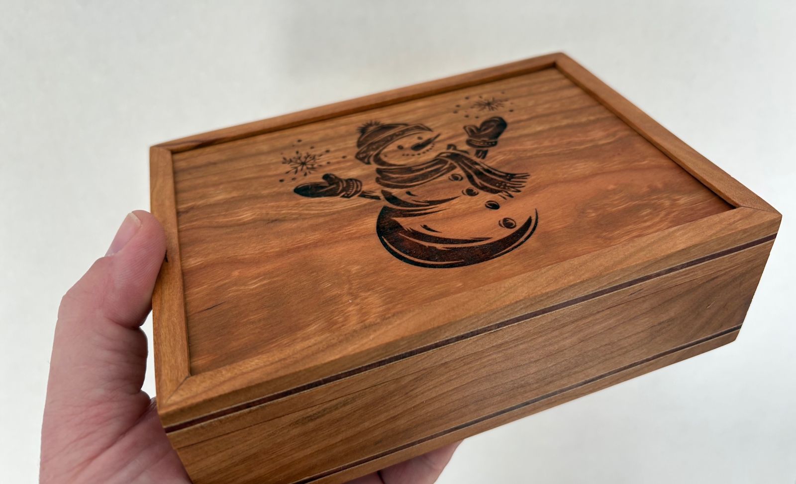 A hand holding a small wooden box, showing scale and how it rests in the palm.